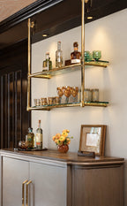 A modern wall-mounted double glass shelf with gold metal framing, styled with bottles and glasses in an elegant interior setting.