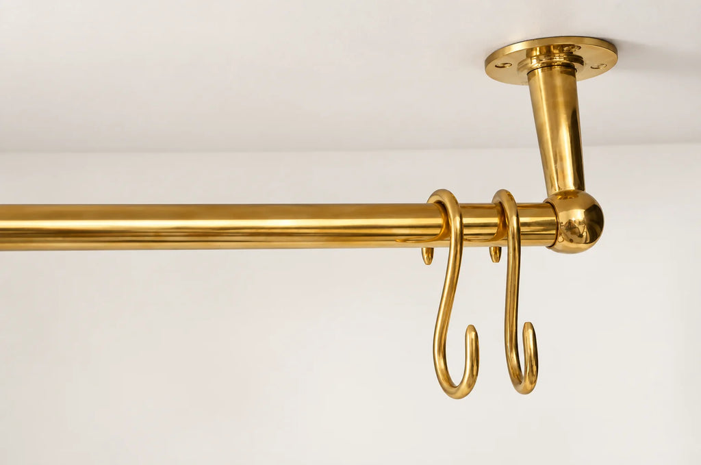 A polished brass hanging rod with two hooks, mounted to a ceiling with a matching ceiling mount, shown against a plain white wall.