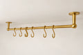 A brass ceiling-mounted clothing rack with six hanging hooks, shown against a plain white wall and ceiling.