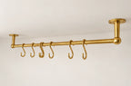 A brass ceiling-mounted clothing rack with six hanging hooks, shown against a plain white wall and ceiling.