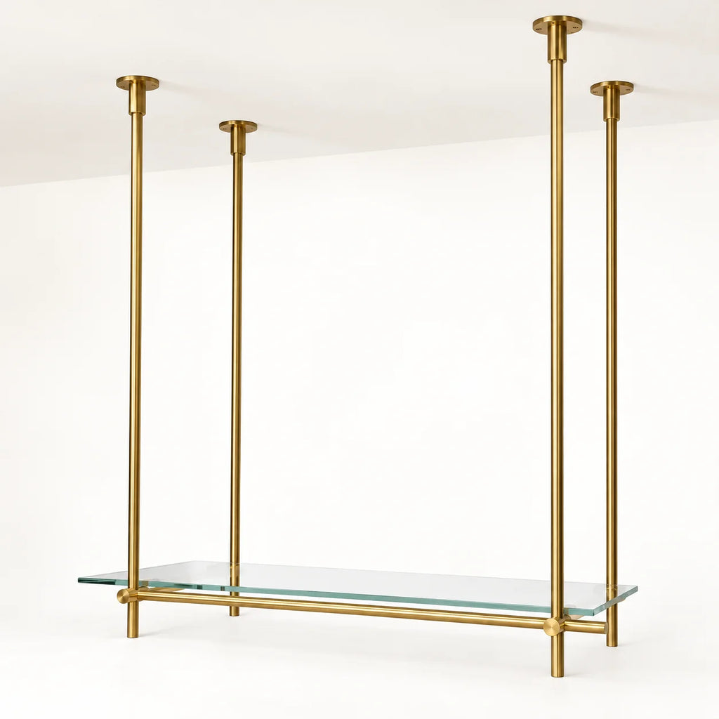 A modern brass wall-mounted shelf with four vertical hanging rods and a clear glass shelf, shown against a clean white wall and ceiling.