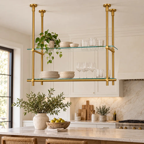 A modern brass double-shelf hanging kitchen island rack with clear glass shelves, styled with dishes and plants in a bright, contemporary kitchen.