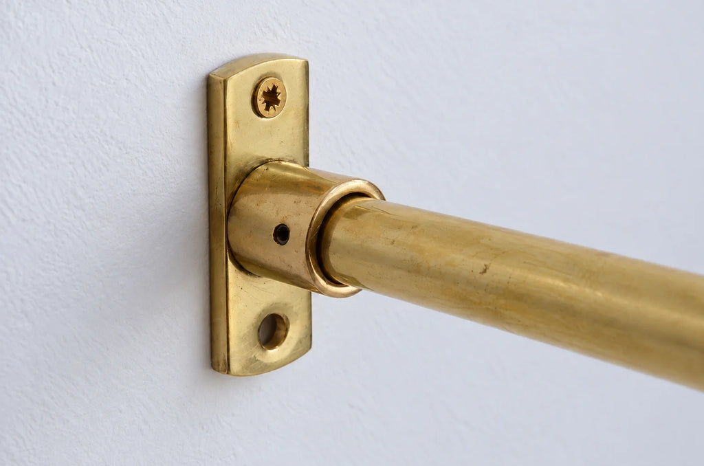 A close-up of a brass curtain rod mounted on a white wall with a matching brass wall plate.