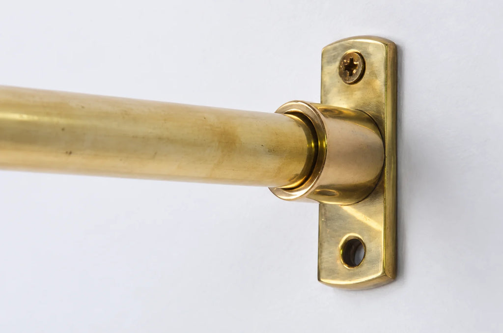 A close-up of a brass curtain rod mounted to a matching brass wall bracket with a screw, shown against a plain white background.