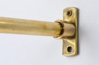A close-up of a brass curtain rod mounted to a matching brass wall bracket with a screw, shown against a plain white background.