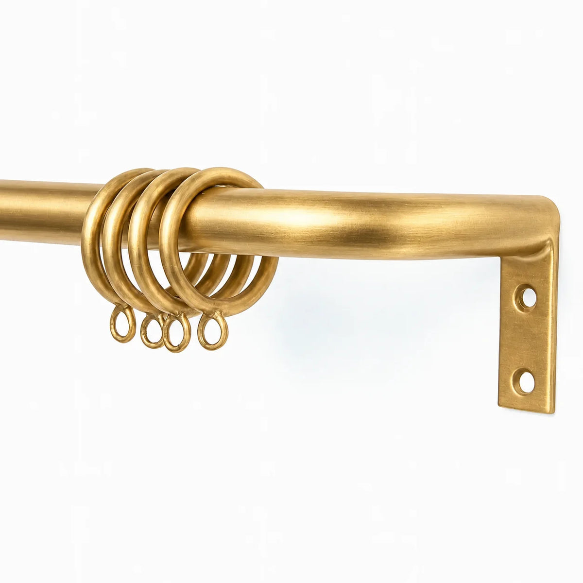 A close-up of a brass curtain rod with a matching metal wall bracket and hanging rings, shown against a plain white background.