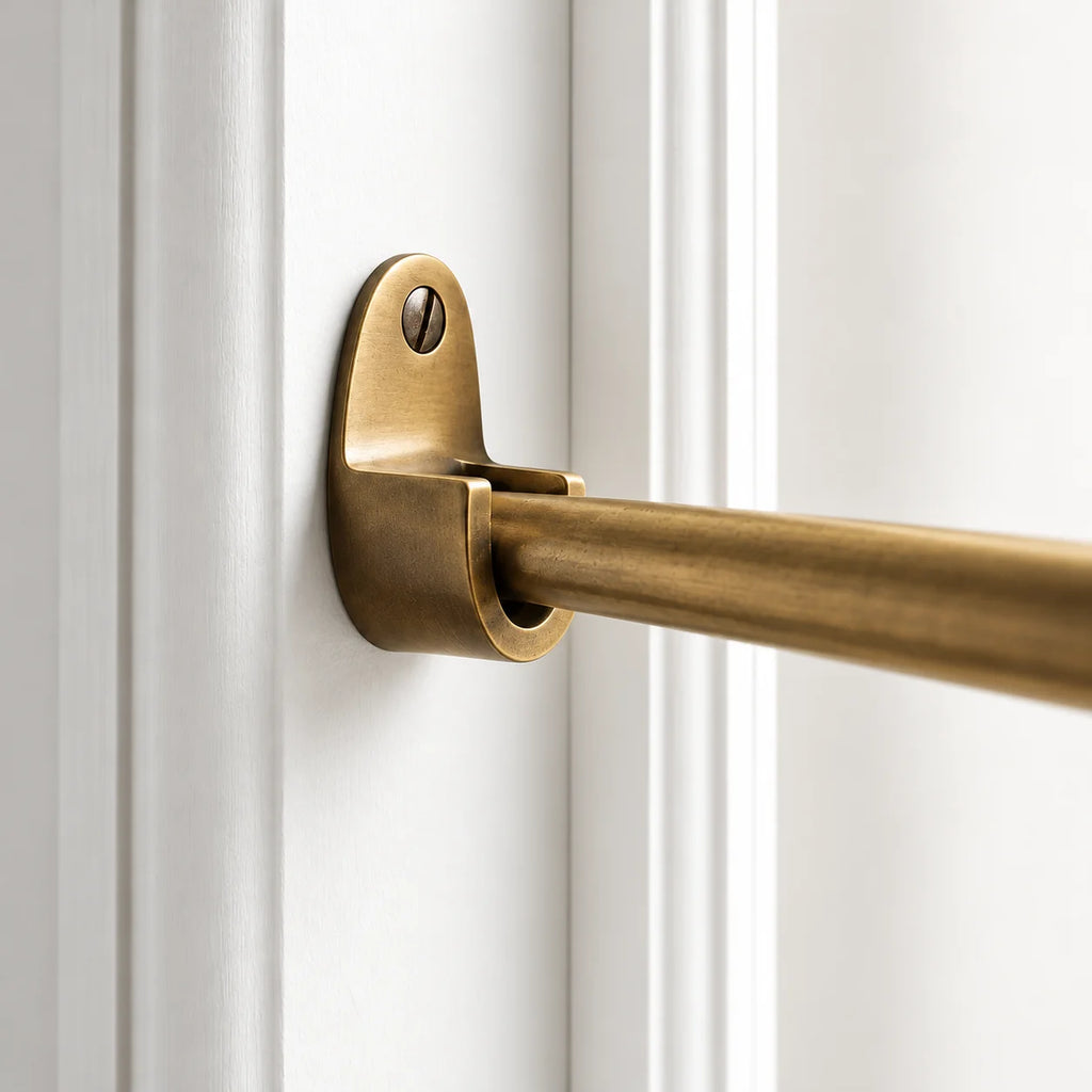Close-up of a brass closet rod hardware mount attached to a white paneled door, with the rod extending to the right.